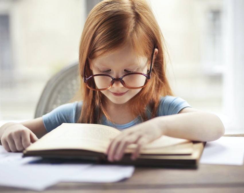 Girl with specs in blue tee shirt reading a book