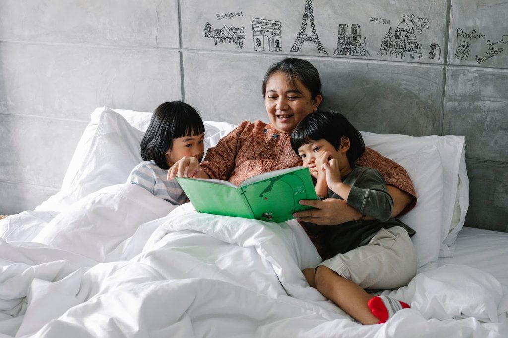 Adorable little siblings reading a book with grandmother on the bed
