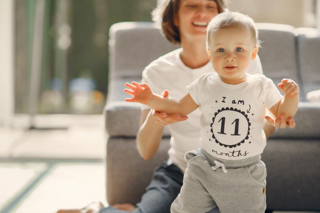 Happy mother helping baby to walk at home