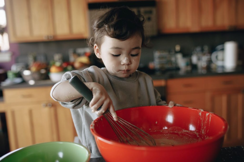 Baby whisking a batter in a red bowl