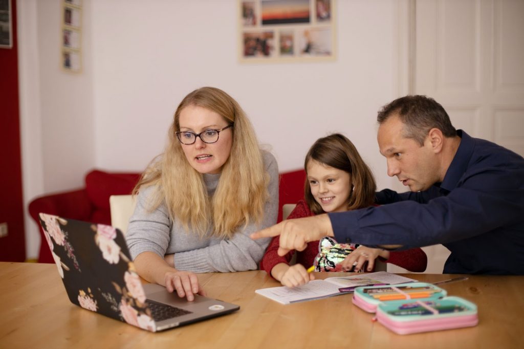 A girl looking at the laptop screen with her parents