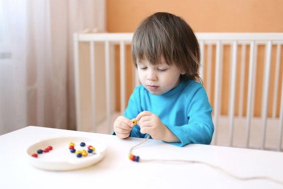 A child stringing a bead in a thread