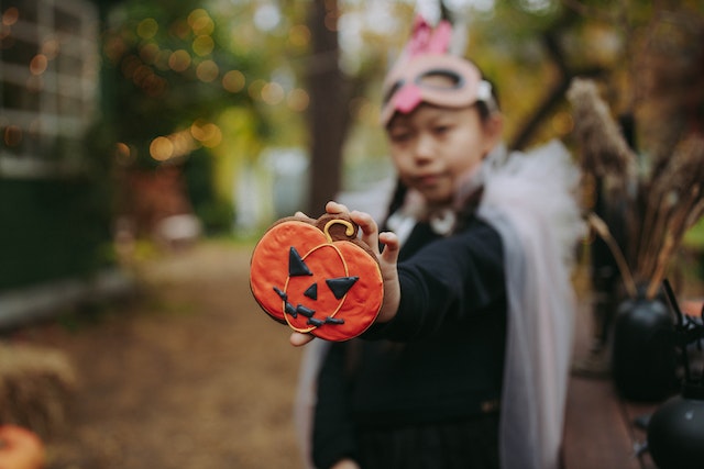 A girl holding a halloween pumpkin themed cookie