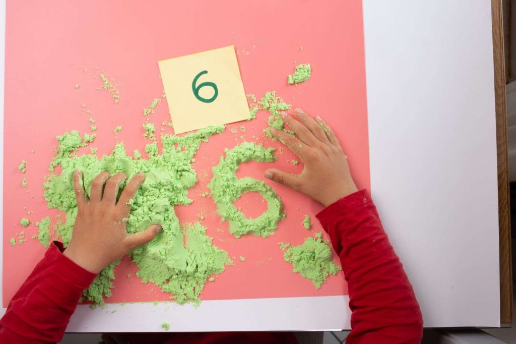 A kid using color sand to write numbers