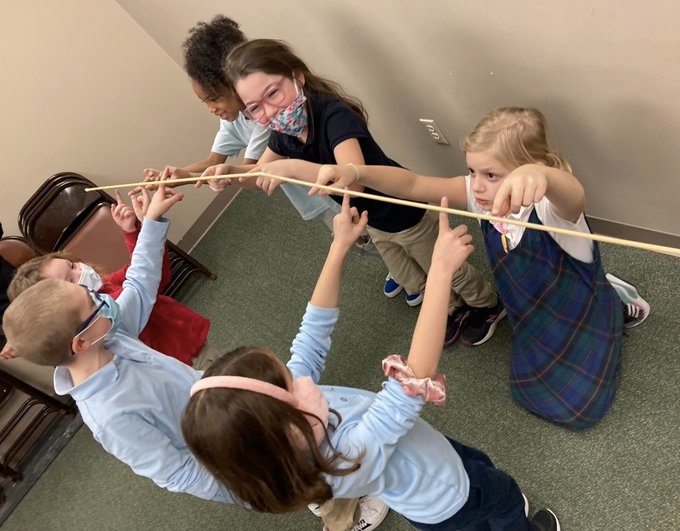 Kids are balancing a stick on their fingers